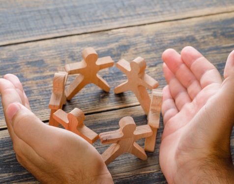 Business success concept on wooden background high angle view. hands protecting wooden figures of people.